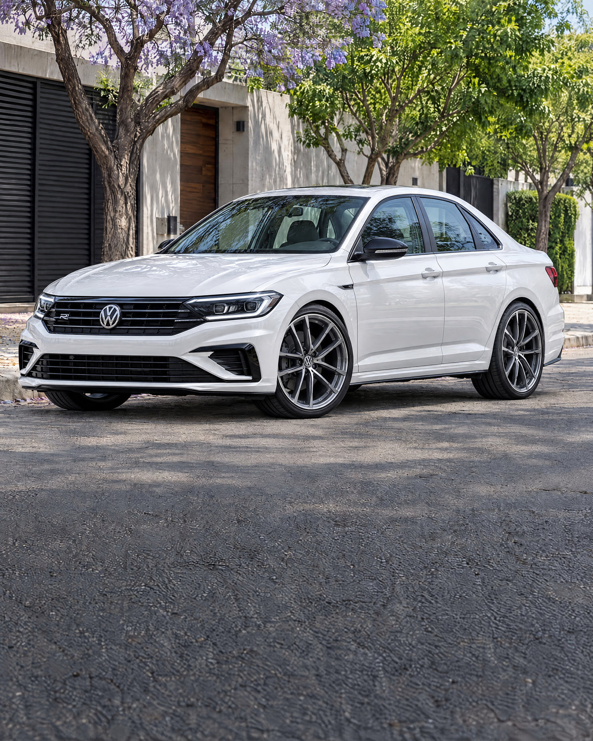 Volkswagen Jetta R-Line blanco con rines deportivos multirradio en una calle arbolada.