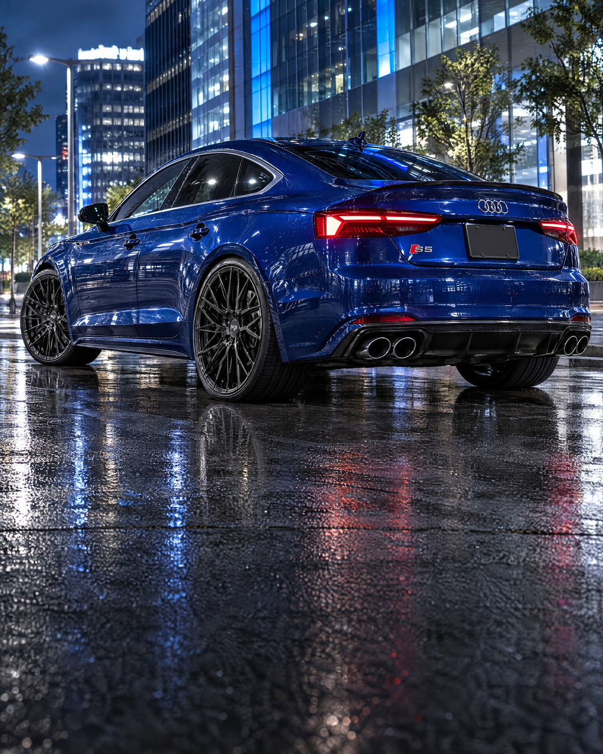 Audi deportivo azul con rines negros en calle nocturna con luces.